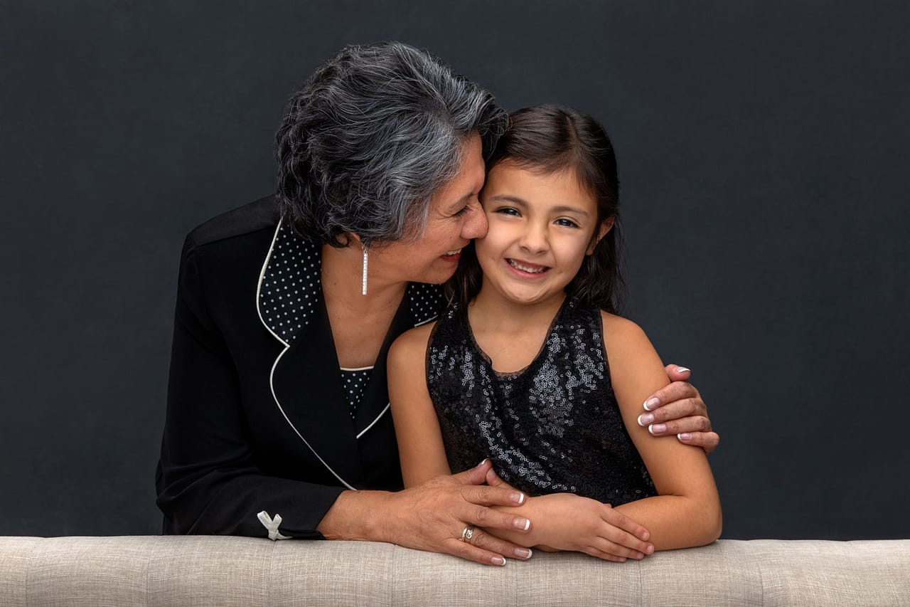 Precious, smiling grandmother and granddaughter snuggling close, grandmother's holding the granddaughter. They are both wearing black. Josh and Stefanie Fraley Family Portrait Photography.