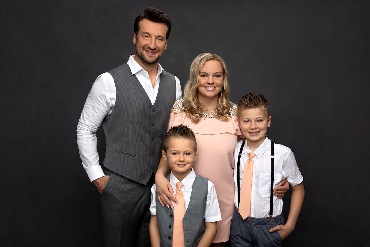 Cute photo of a family of four, dad, mom and two boys standing close to each other. They are color coordinated with peach, white and gray. Family Portrait Photography.