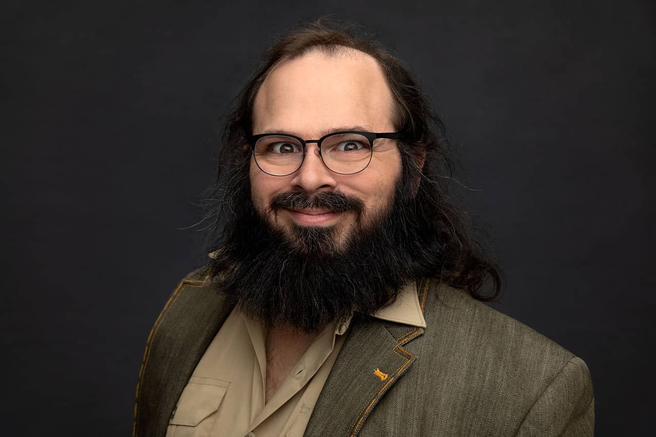 Mischievous photo of an actor playing the mad scientist character with wild hair. Wide eyed and wearing a green shirt with green jacket. Jonathan Hano Acting and Headshot Photography.