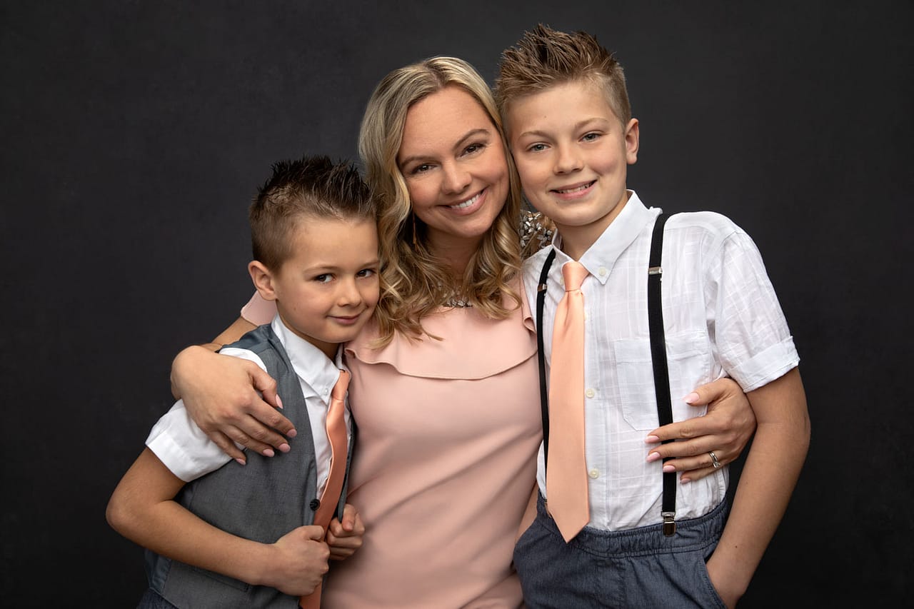 Precious photo of a mother with her two boys. She is holding her two sons close, with her arms around them. They are color coordinated with peach, white and gray. Family Portrait Photography.