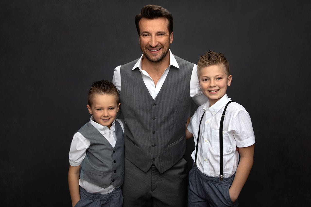 Cute photo of a father and his two sons standing with arms around each other. They are color coordinated with white and gray. Family Portrait Photography.