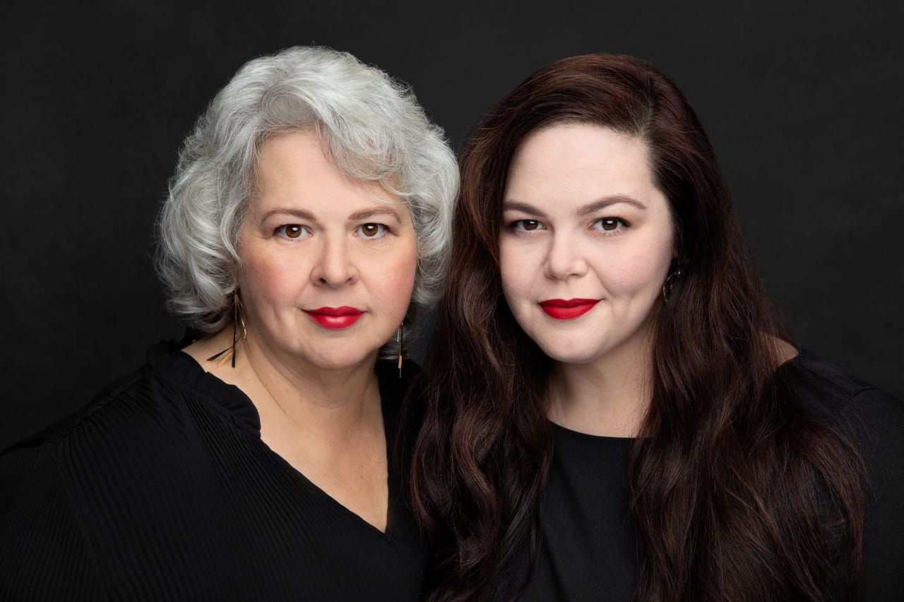 Beautiful photo of a beautiful mother and daughter together. The mother has beautiful silver hair and red lipstick. The daughter has long brown hair and red lipstick. Veronica Pitre Women's Portrait Photography.