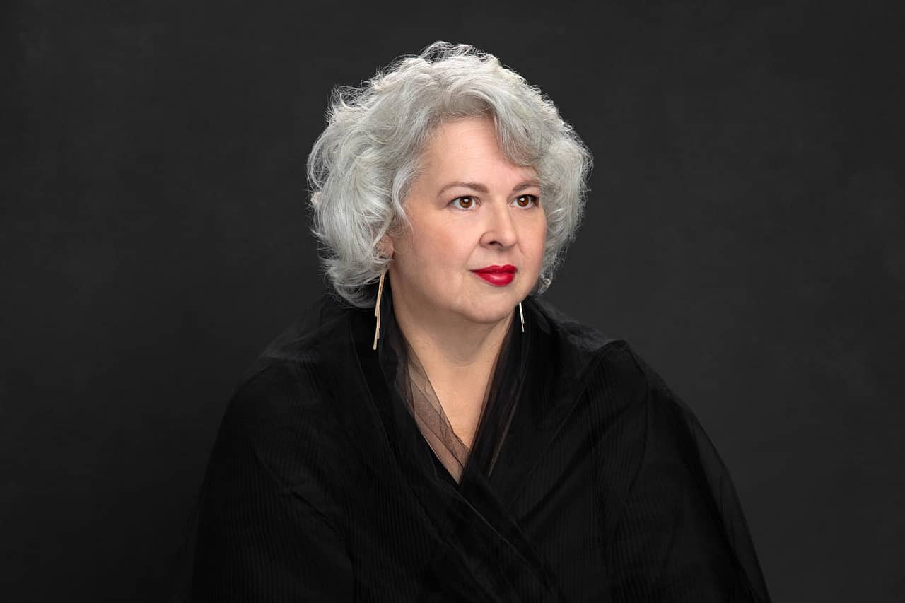 Elegant photo of a beautiful woman. She has beautiful silver hair and red lipstick. She is wearing a black shirt and black toole Veronica Pitre Women's Portrait Photography.