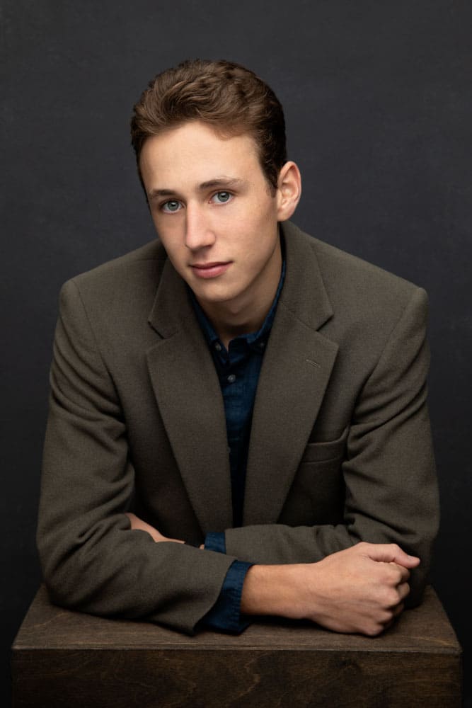 Nice photo of a handsome young man leaning forward wearing a muted green jacket. Don and Beverly Elmore Family Portrait Photography.