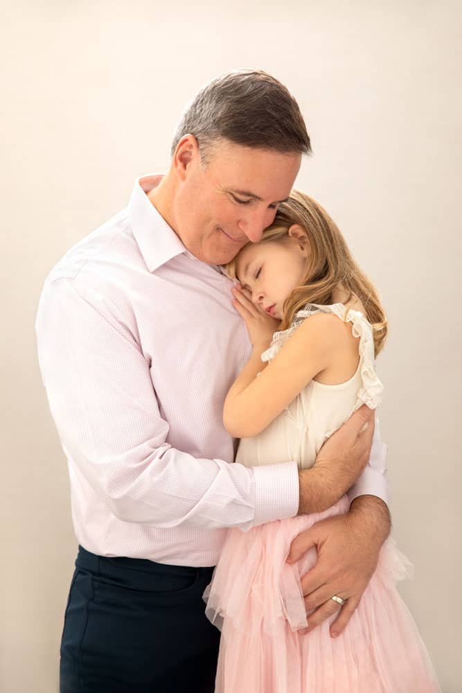 Precious photo of a father and daughter standing and holding each other. The daughter, who has blonde hair, is resting her hand on his chest and snuggling close. Chris and Amber Edwards Family Portrait Photography.