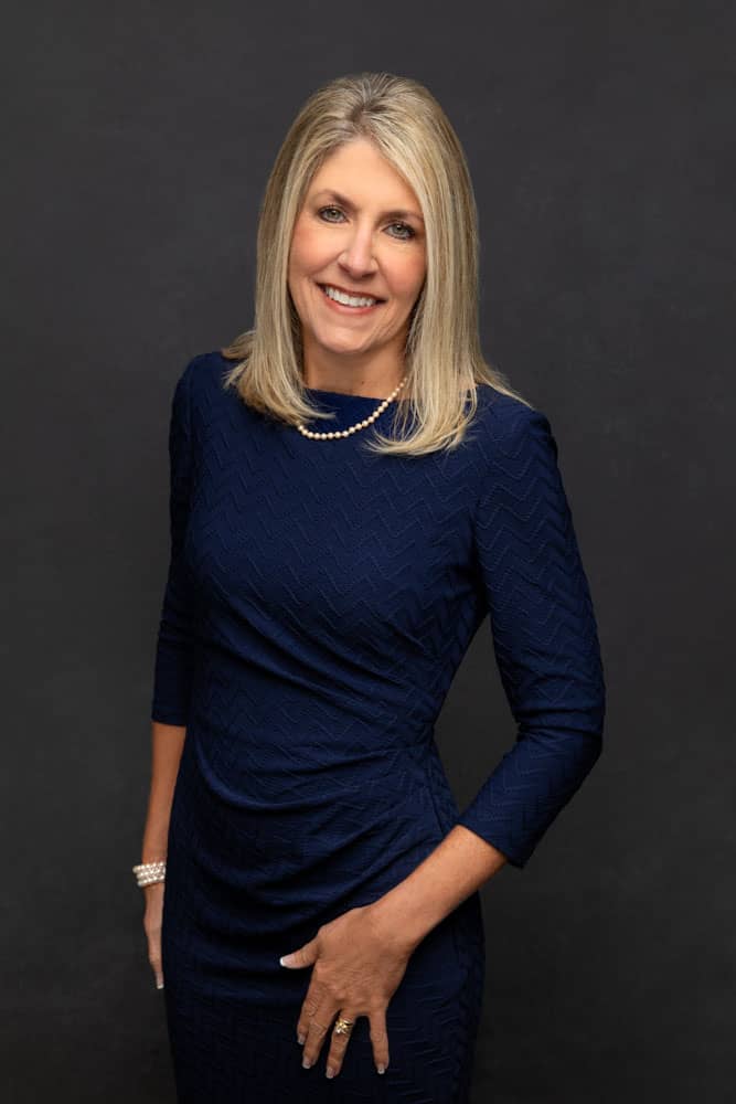 Nice photo of a pretty, smiling woman with blond hair, a blue dress and a pearl necklace. Don and Beverly Elmore Family Portrait Photography.