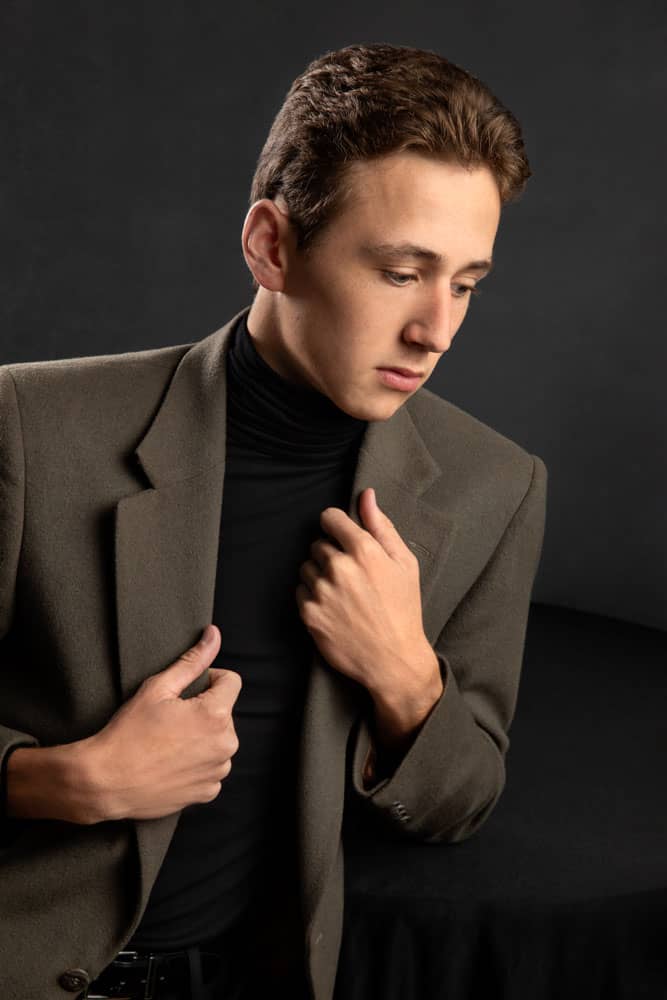 Nice photo of a handsome high school senior with a muted green jacket and black shirt. His hands are holding the collars of his jacket. Elmore Senior Portrait Photography.