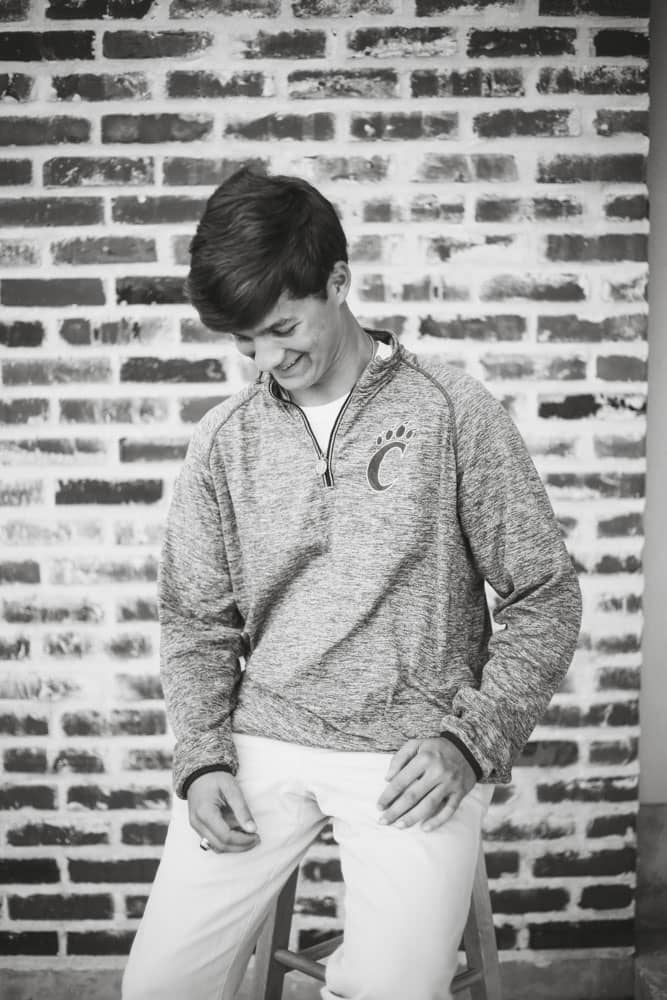 Senior photo of a young man graduating. He's wearing a school sweater and sitting on a stool. Thomas Evans Senior Portrait Photography.