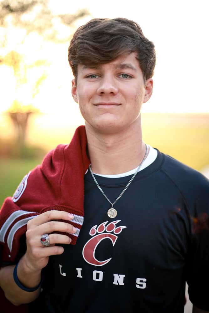 Senior photo of a young man graduating. He's wearing a school ring and school shirt, with his letterman jacket resting over his shoulder. Thomas Evans Senior Portrait Photography.