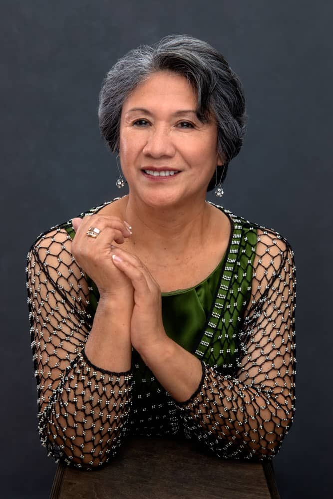 Classy photo of a beautiful smiling grandmother with beautiful silver and black hair. Holding her hands close, she is wearing a green shirt, pretty rings and earrings. Josh and Stefanie Fraley Family Portrait Photography.